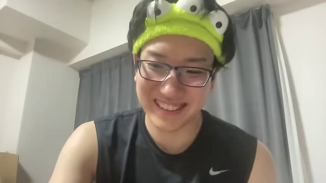 緑色の帽子をかぶったみつおが、暑い部屋について話している本人カメラ画面