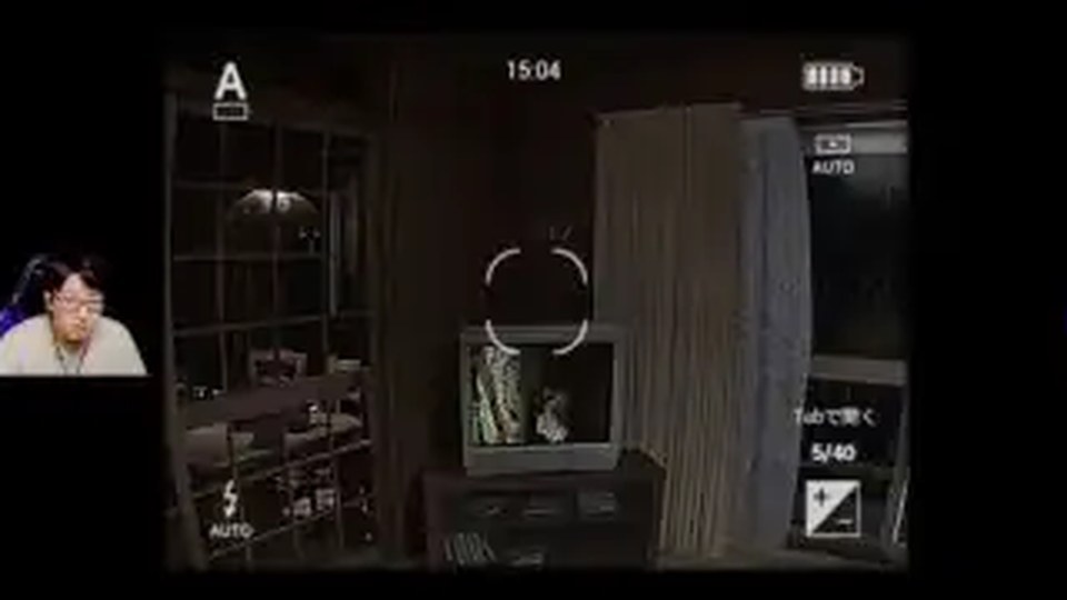 暗い室内でカメラをテレビに向けるホラーゲームの画面
