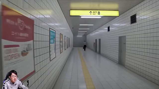 8番出口の白いタイルの通路で、黄色い出口8の案内板と遠くに立つ男性を見るみつお