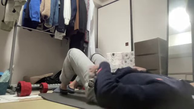 床に寝て腹筋をするみつおとそばに置かれた赤いダンベル