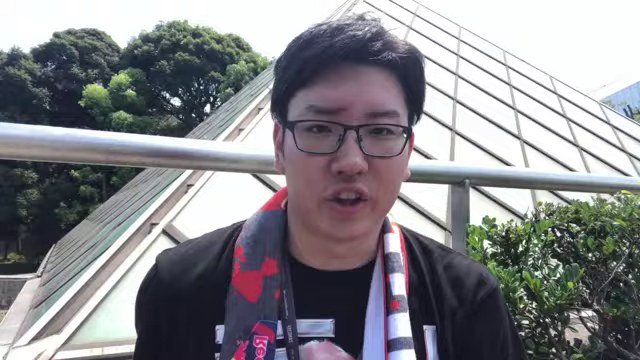 屋外で赤と白のマフラーを掛け、カメラに向かって対戦を振り返るみつお