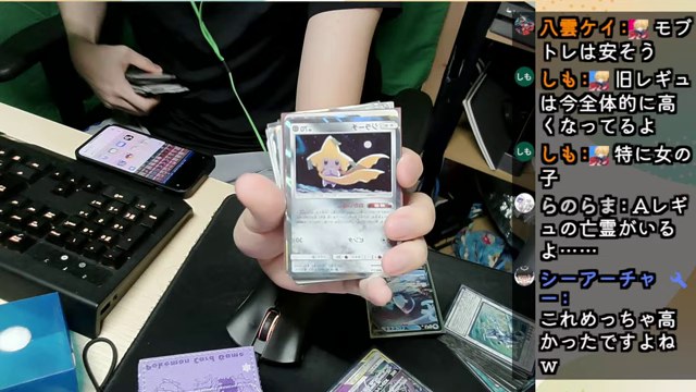 机にポケモンカードを広げ、一枚をカメラに向けているみつお