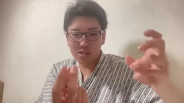 ホテル室内の配信で、みつおが両手でコップの大きさを示すように話している