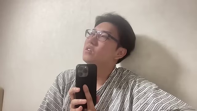 ホテル室内の配信で、みつおがスマートフォンを手にカードショップの様子を説明している