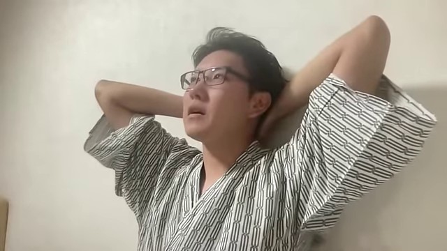ホテル室内の配信で、みつおが両手を頭の後ろに置いて帰りの予定を話している
