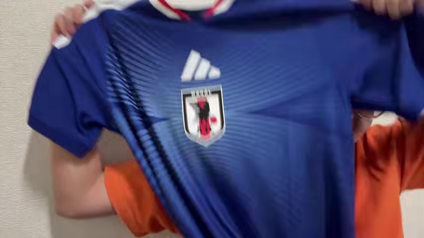 みつおがカメラに広げて見せる青いサッカーのユニフォーム