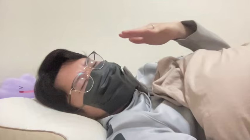 布団に横になり、マスクと眼鏡を着けてカメラに話すみつお