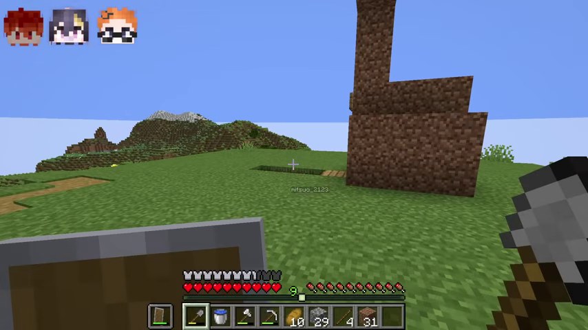 マインクラフトの草原に土でできた背の高い建物が映る場面