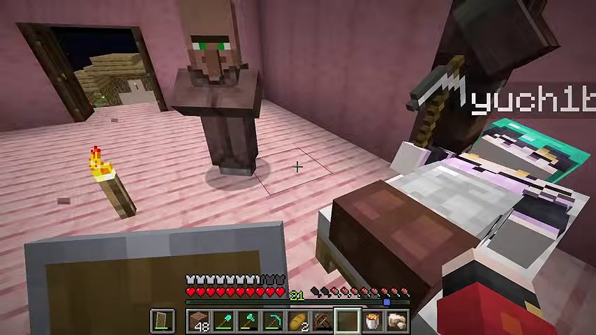 マインクラフトのピンクの家で、ベッドに横たわるゆうちびさんのそばに村人が立つ場面